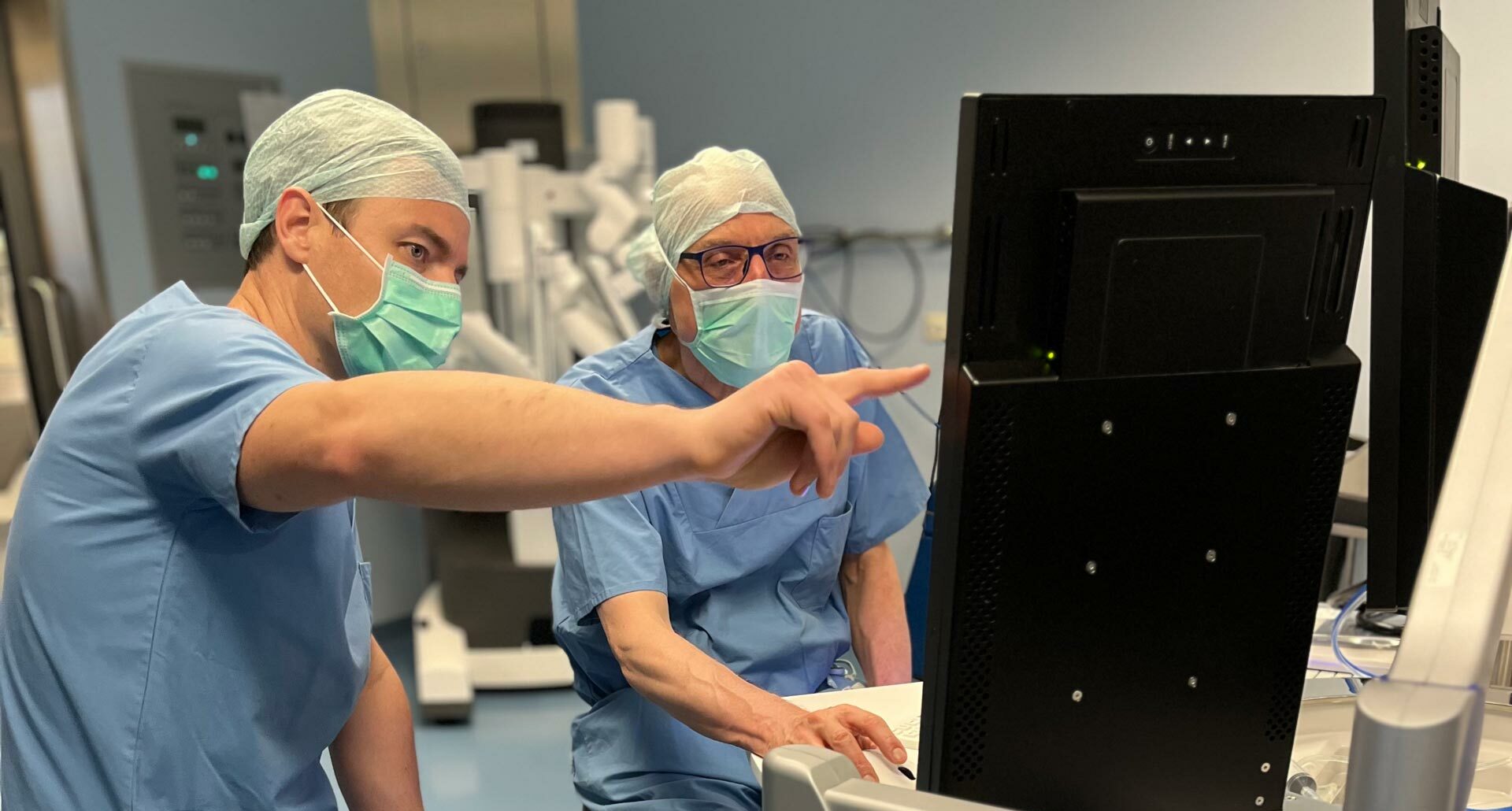Zwei Chirurgen im Operationssaal betrachten einen Monitor, einer zeigt auf die Anzeige.